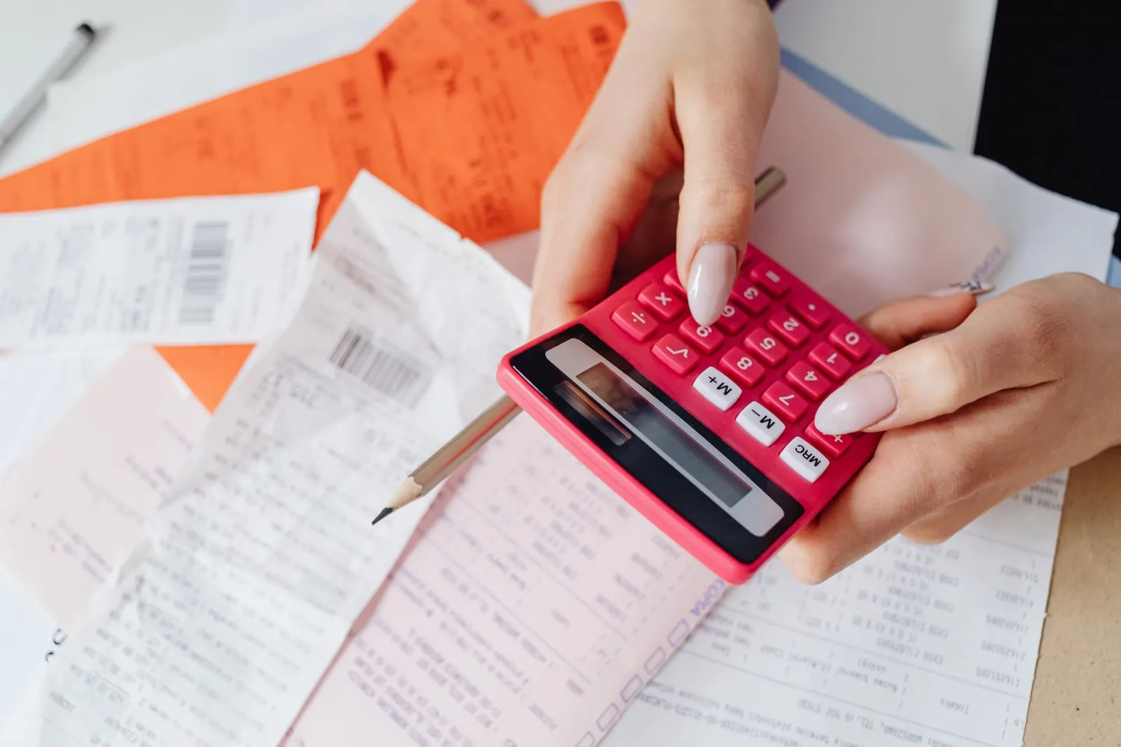 Hands holding a calculator over a spread of receipts and invoices