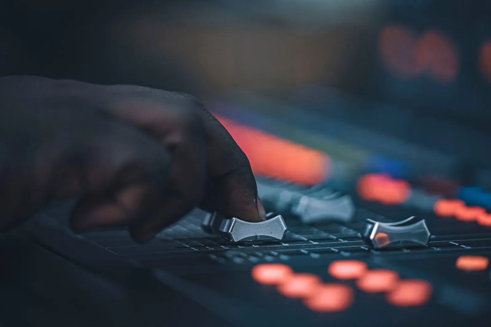 A hand adjusting a fader on an audio mixing desk