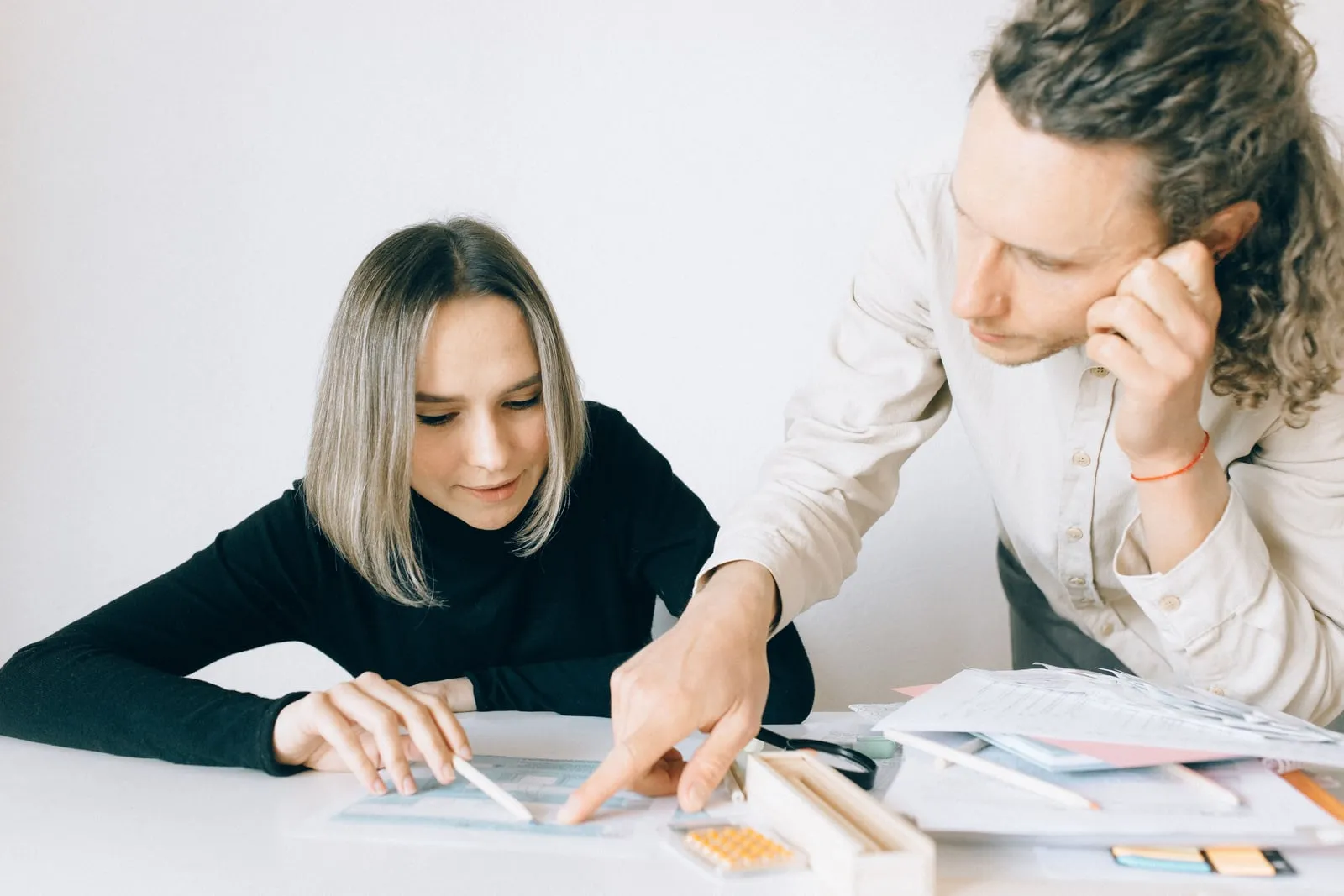 Two office workers at a shared desk discussing paperwork