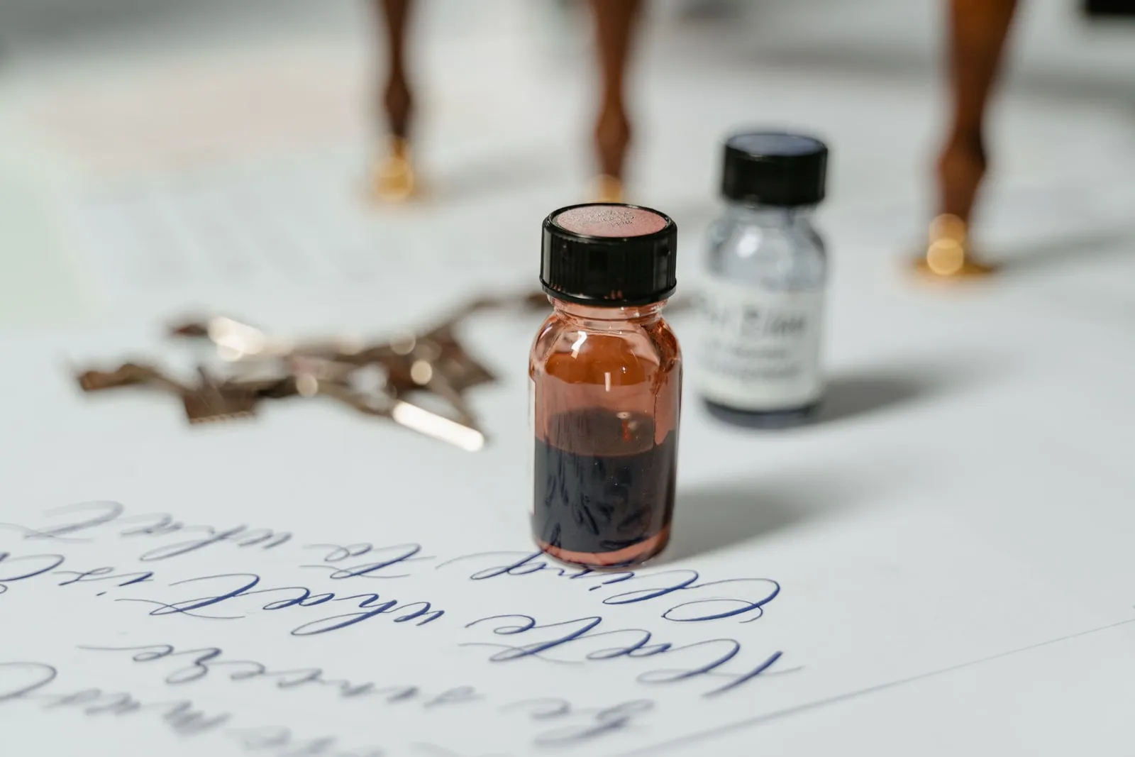 Bottles of ink and calligraphy nibs beside a sheet of handwriting