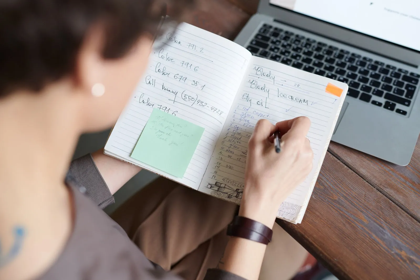 A person writing notes beside a laptop at a desk