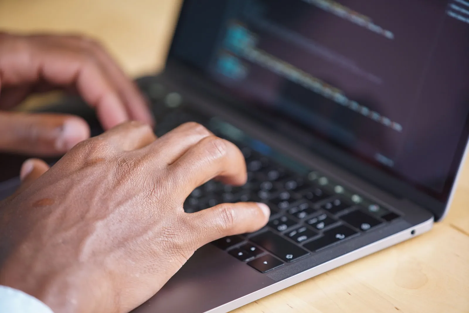 Hands typing on a laptop keyboard with code on the screen