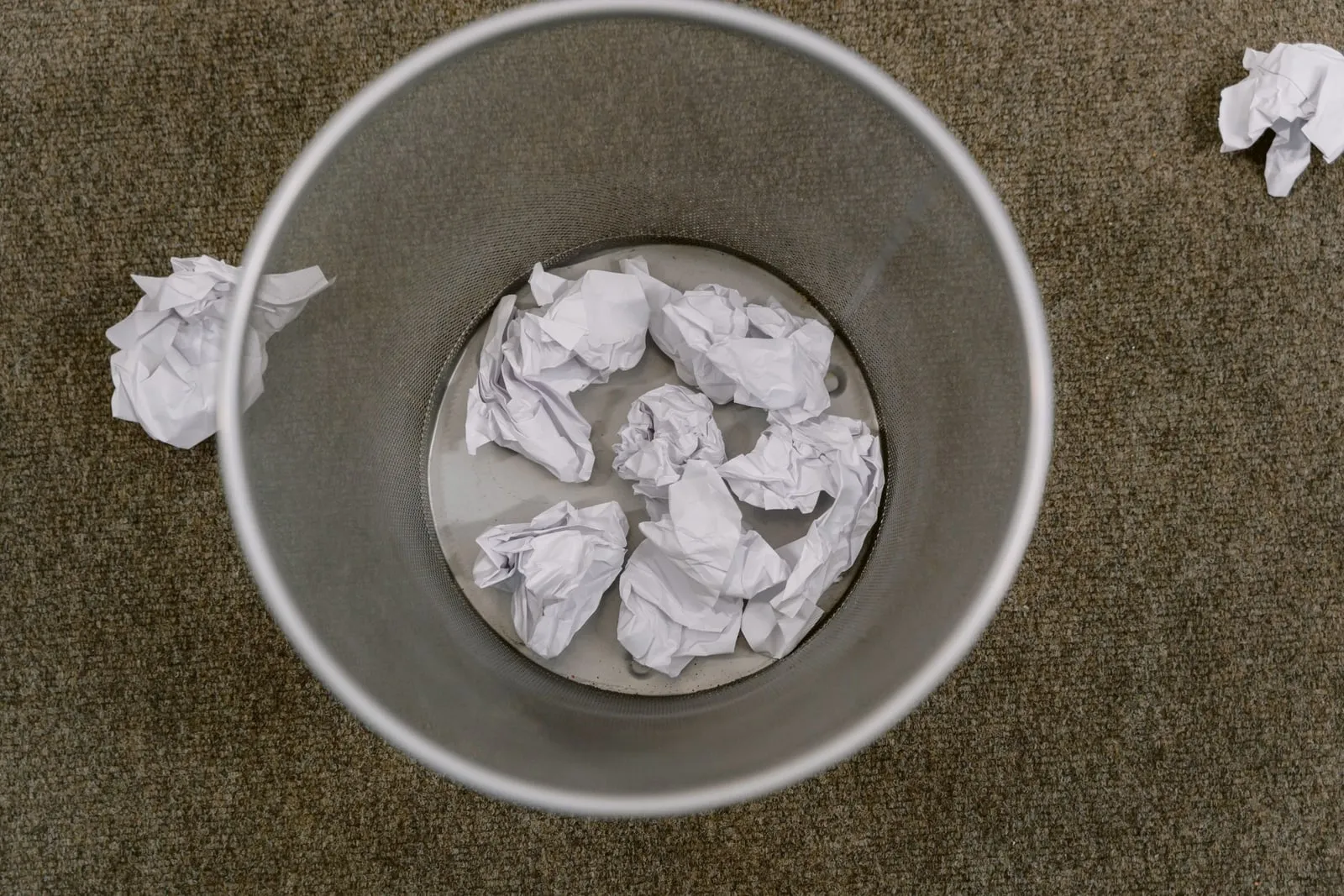 Crumpled paper balls in and around a wastebasket seen from above