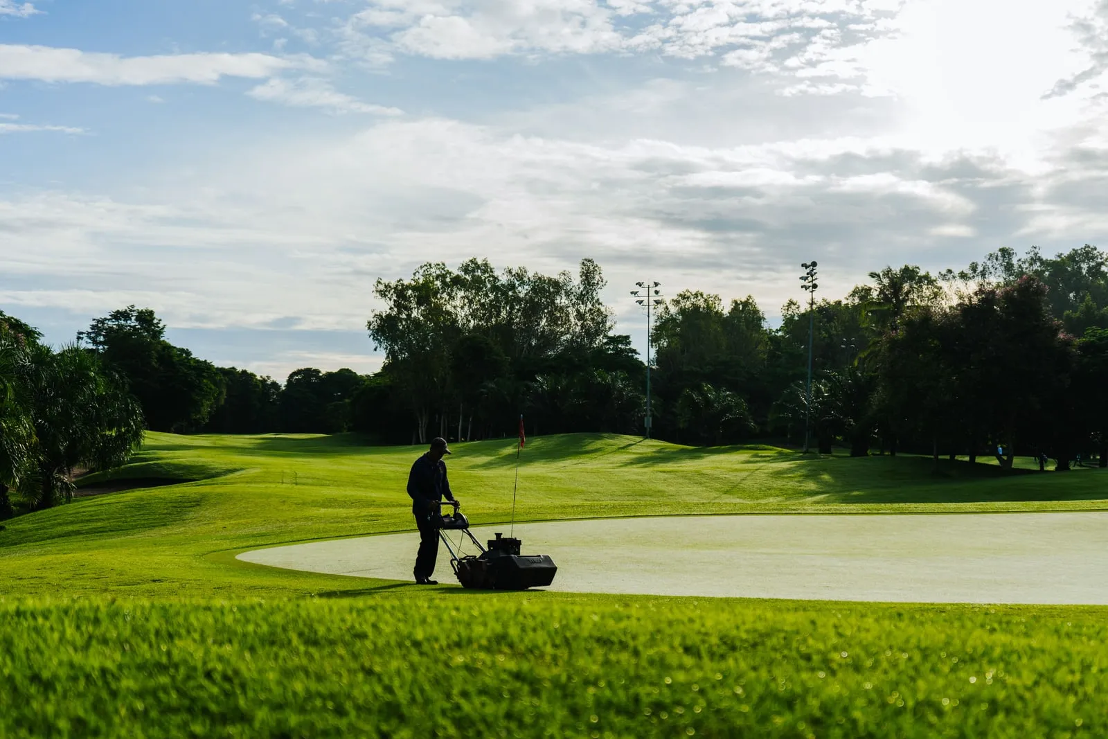 A groundskeeper mowing a green on a golf course in the morning.