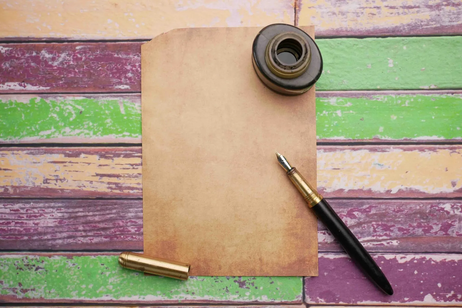 A fountain pen and an ink pot beside a blank sheet of aged paper