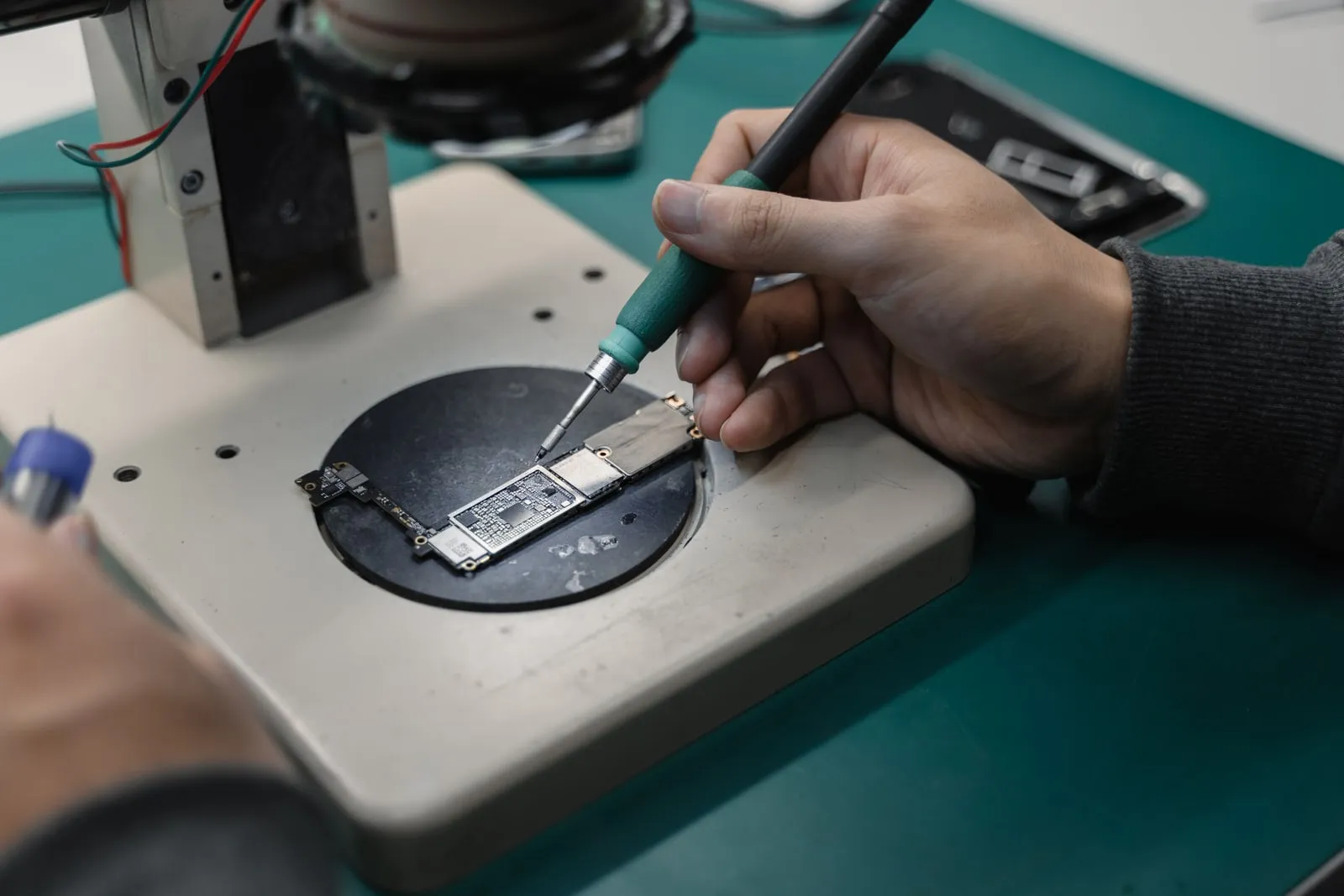 A technician working on a circuit board under a bench microscope