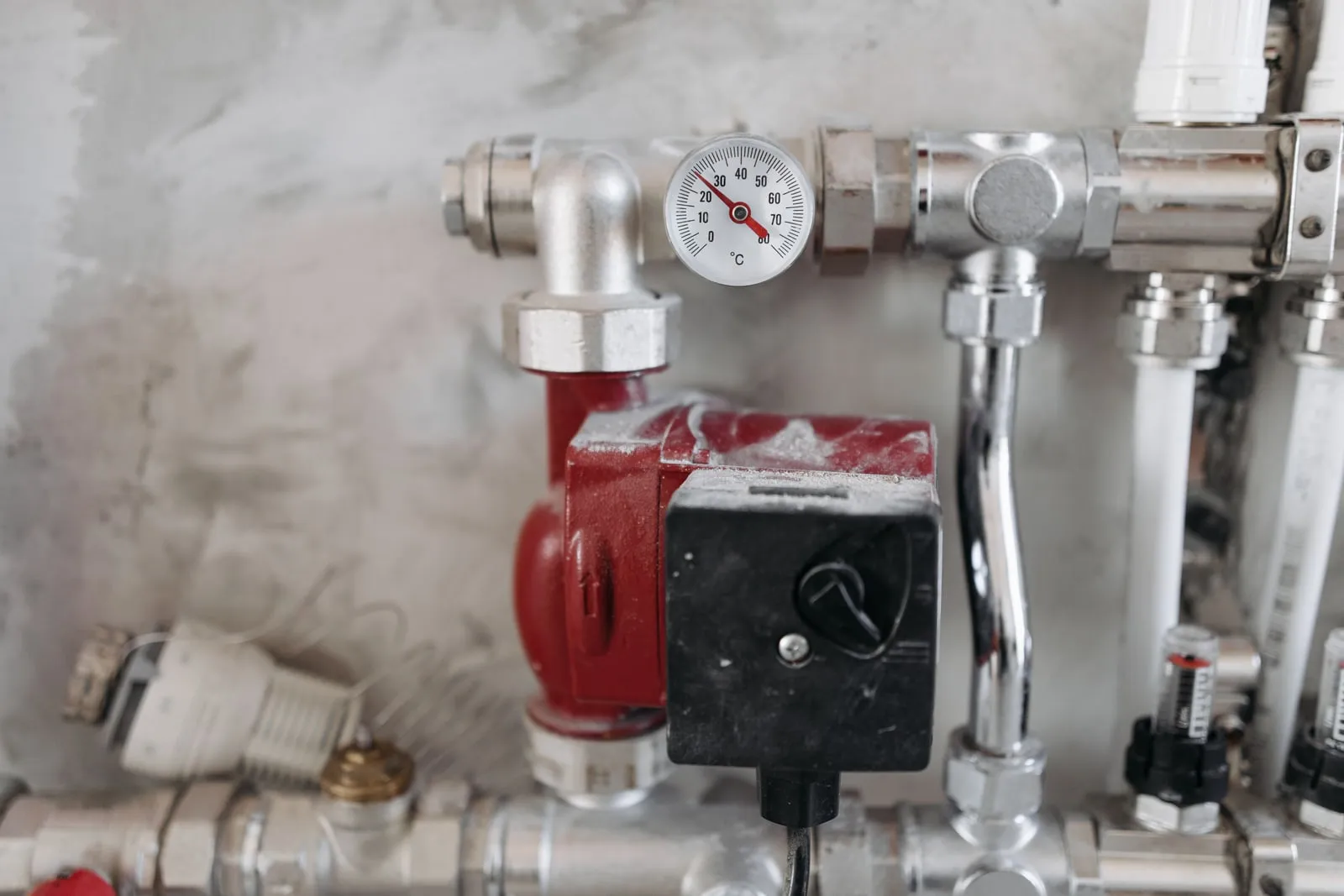 A temperature gauge and a red circulation pump on a metal pipe manifold