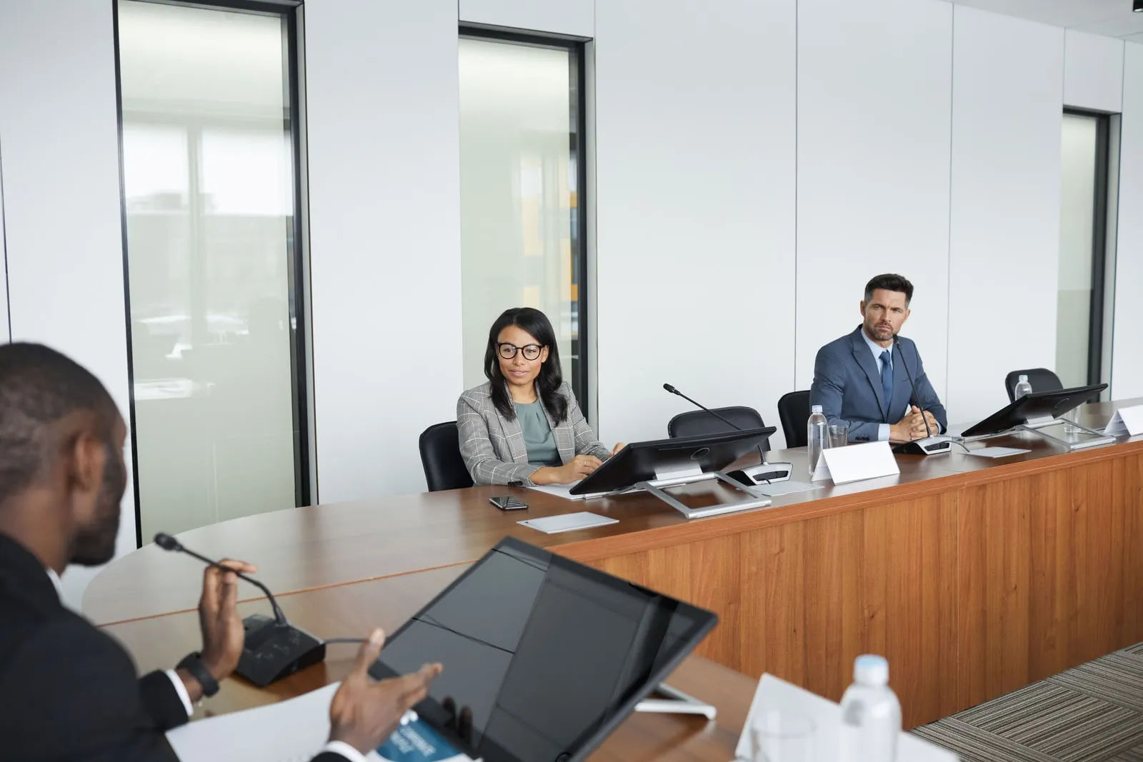 Three people at a curved conference table with microphones and monitors