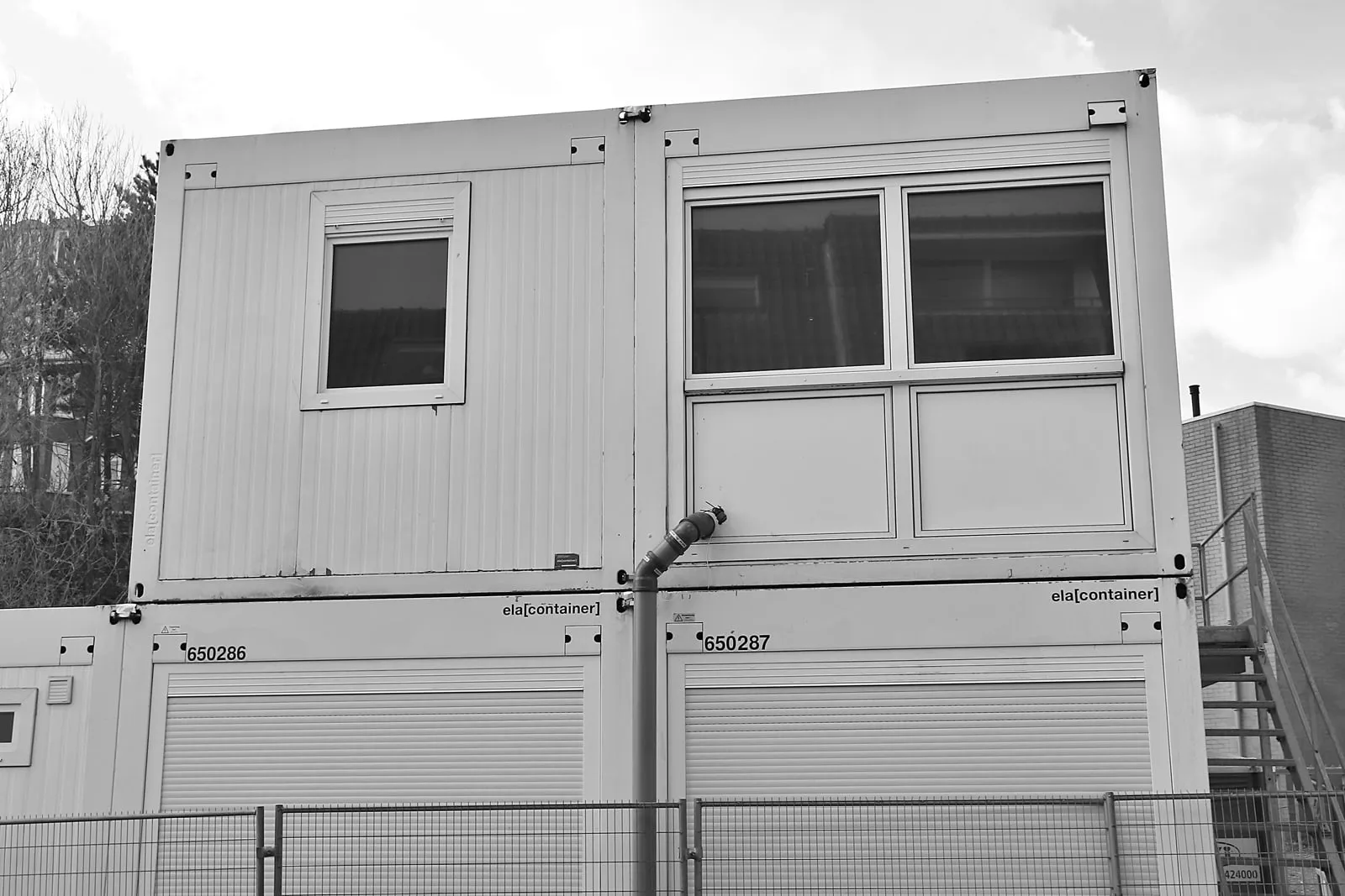Stacked prefabricated cabin modules behind a site fence