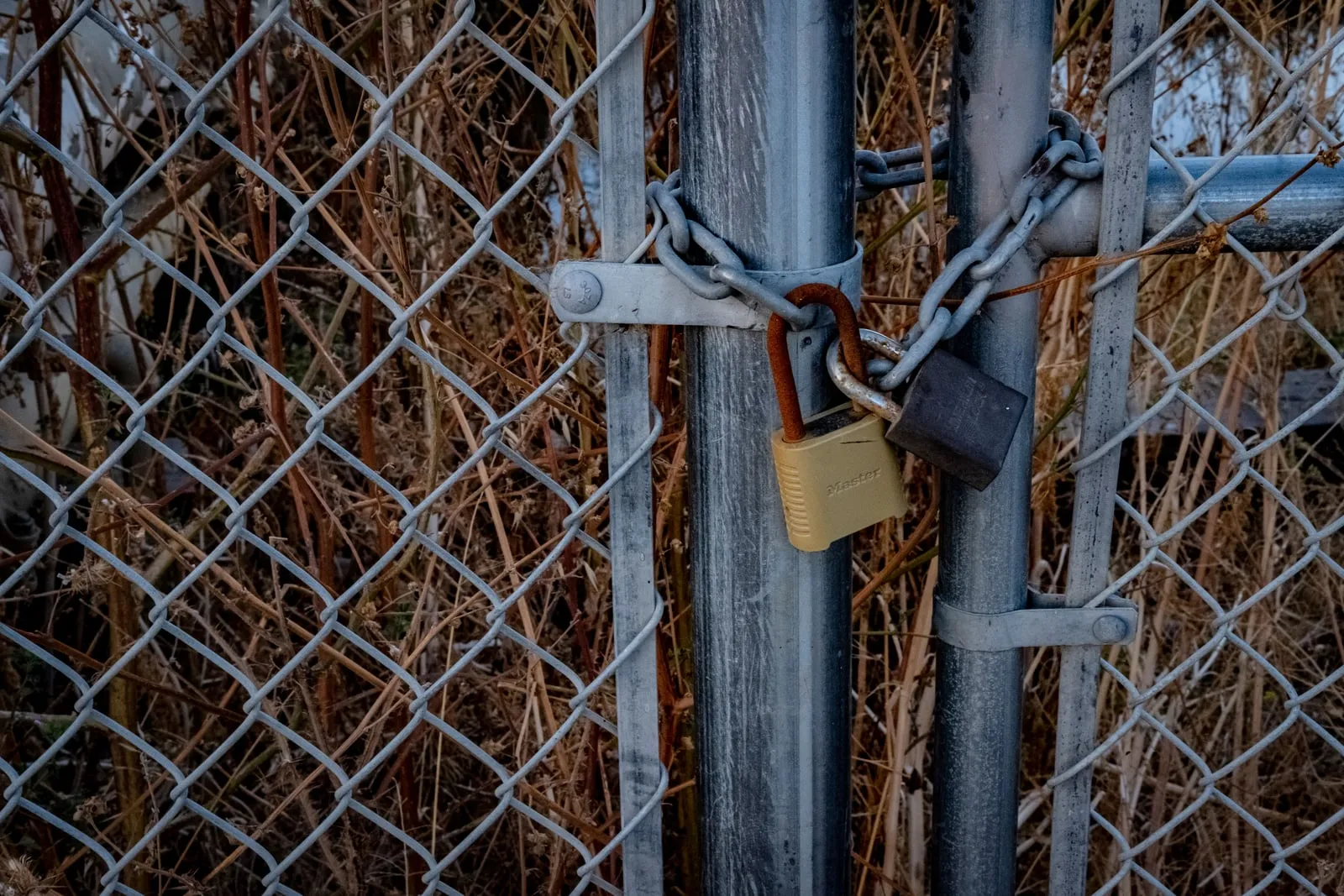 Two padlocks and a chain fastening a chain-link gate