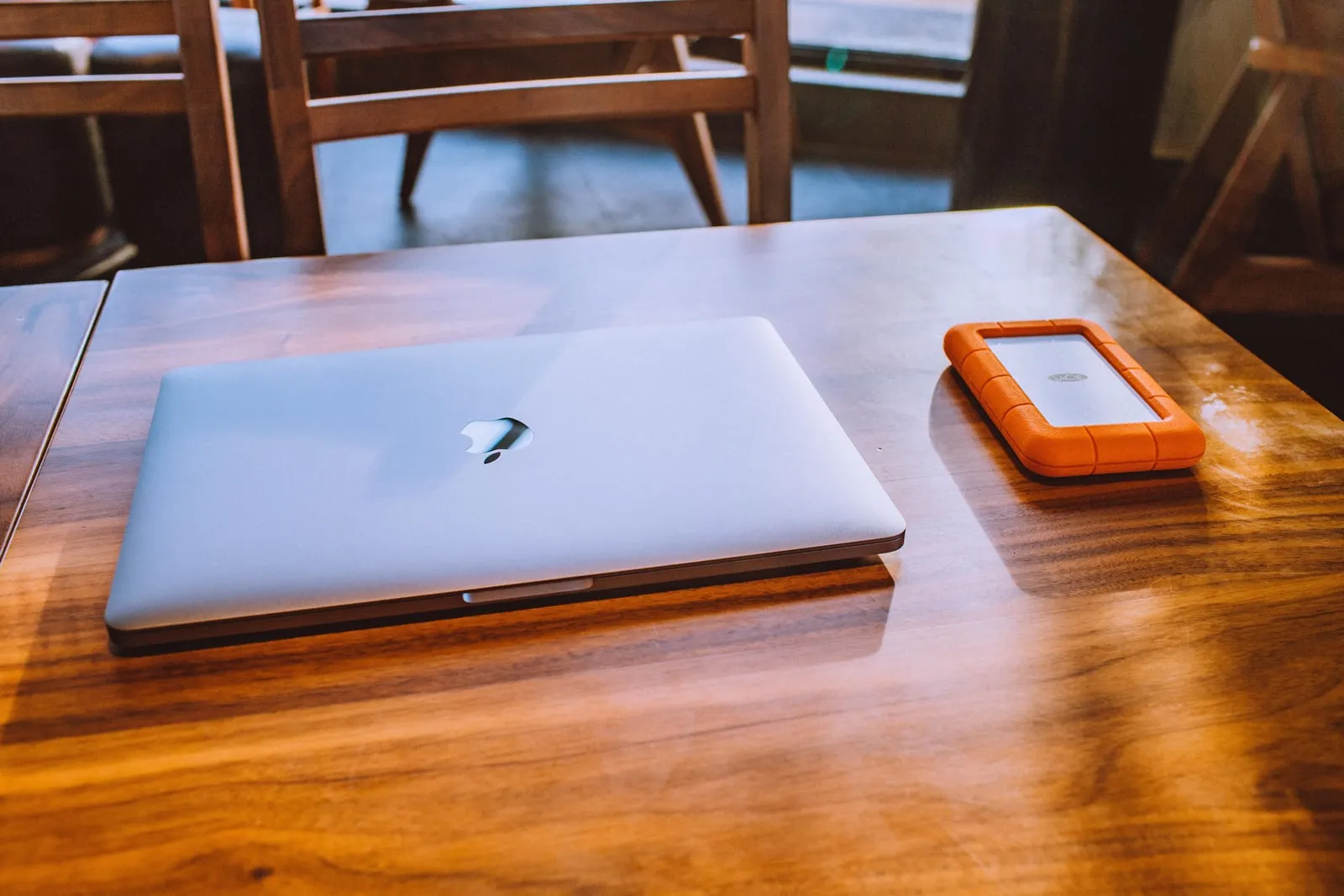 A closed laptop beside a rugged external hard drive on a wooden table