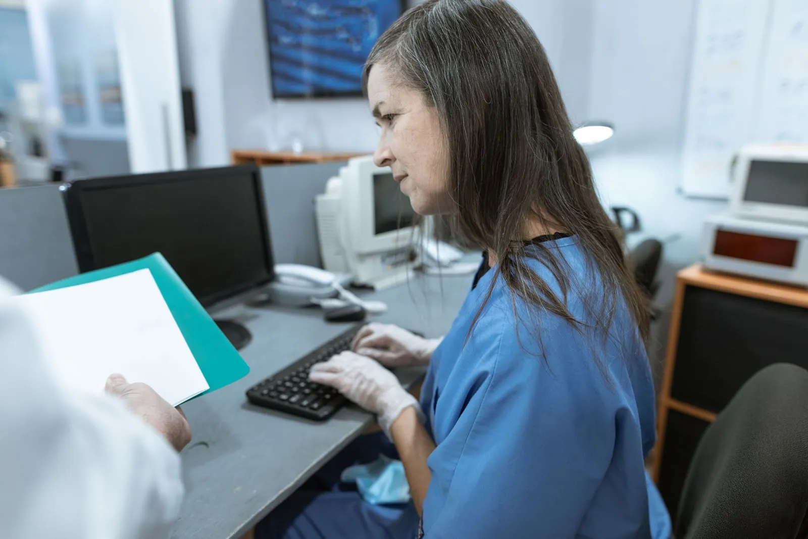 Clinician in blue scrubs typing at a hospital computer