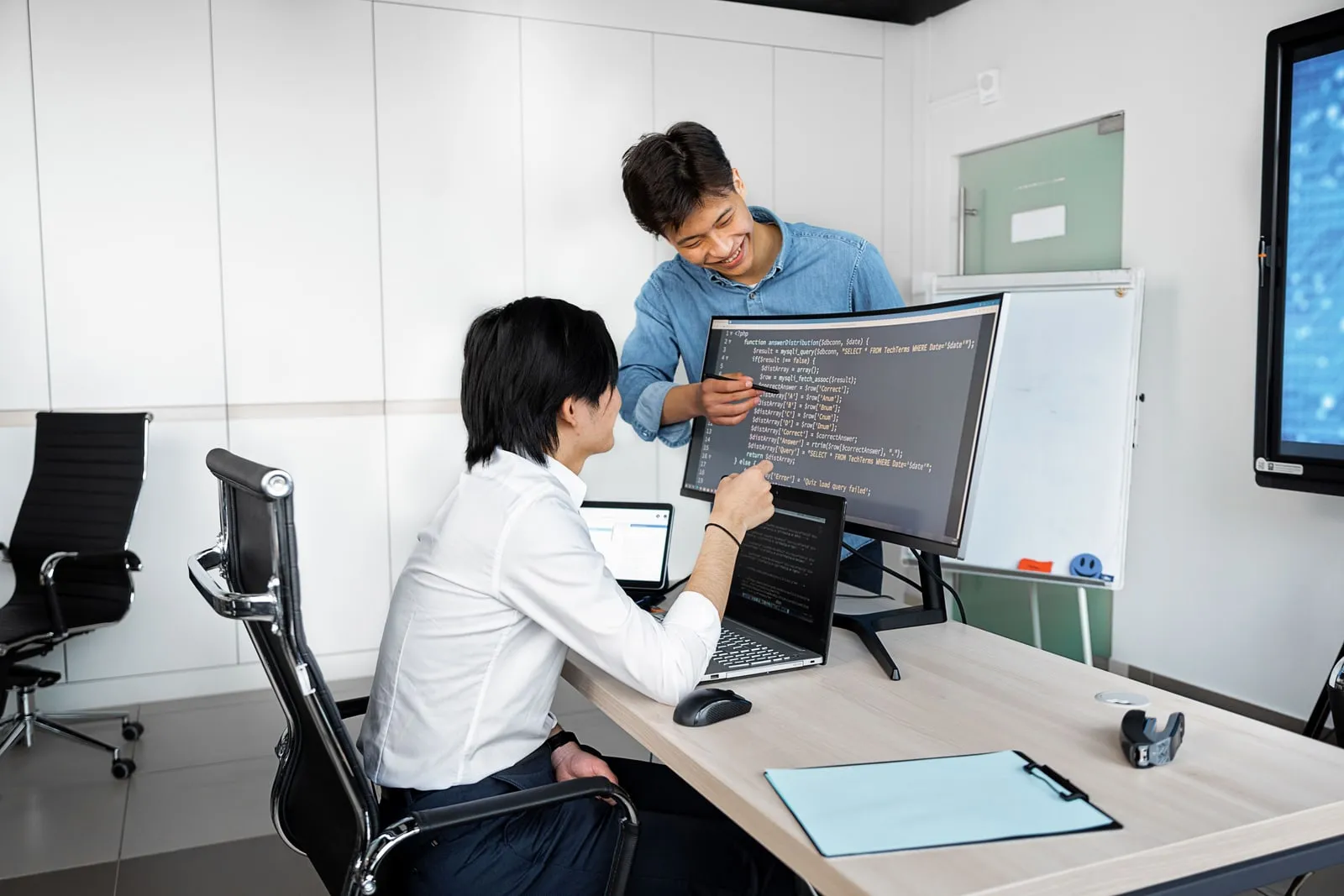 Two colleagues looking at code on a large monitor in an office
