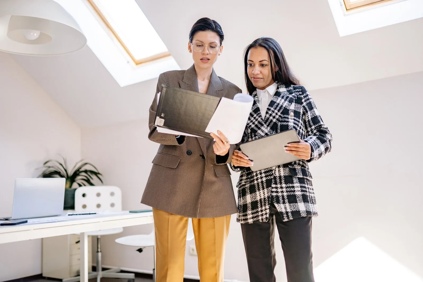 Two colleagues standing in a bright office, looking through a document together