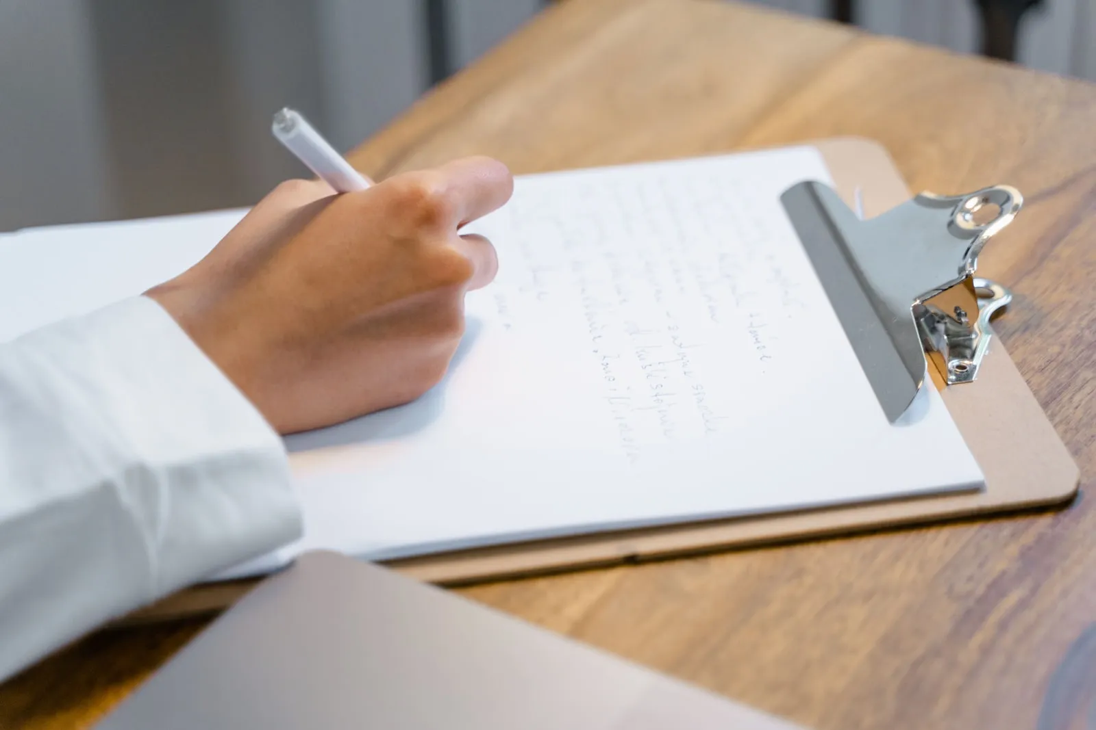 A hand writing on a clipboard resting on a wooden table