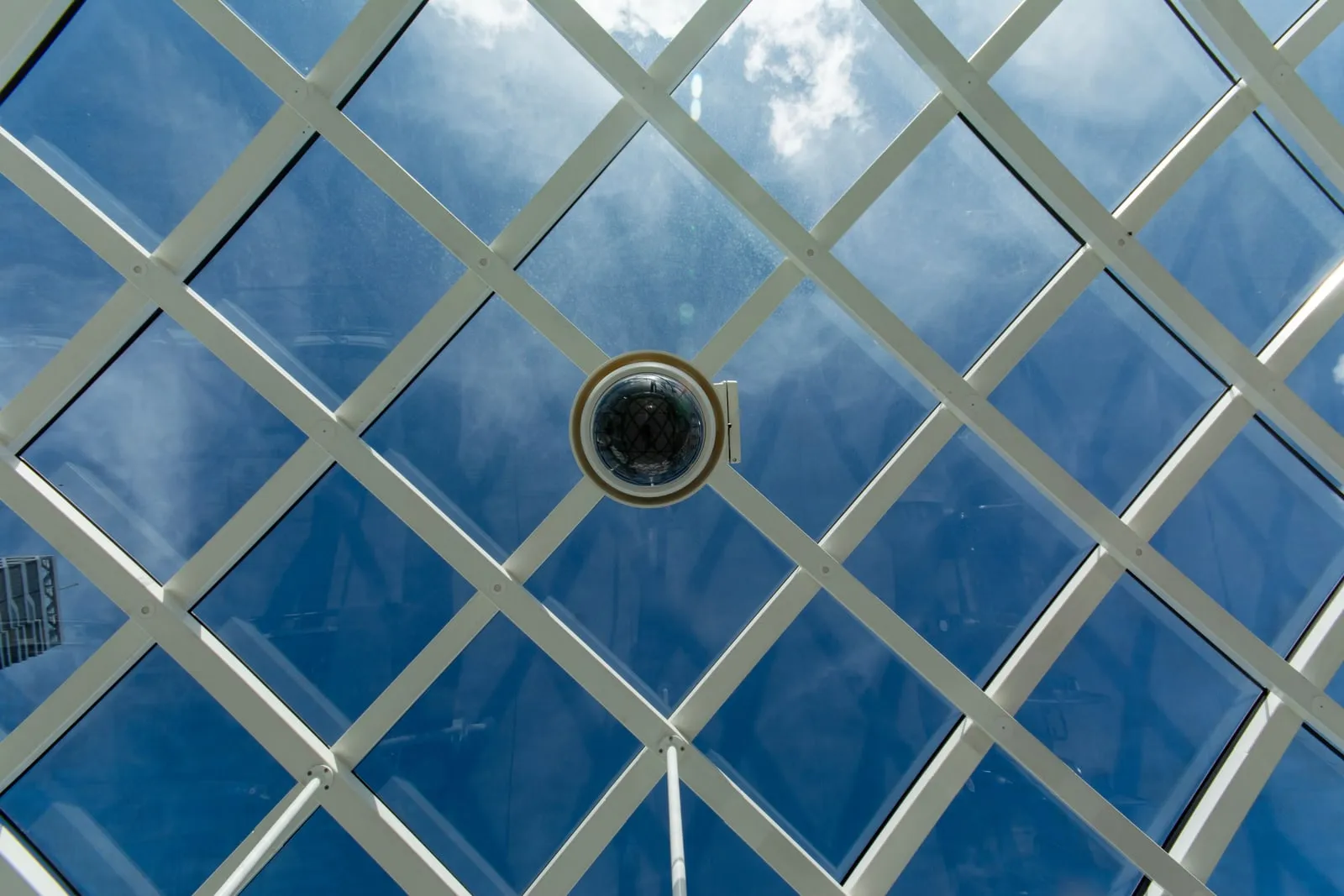 A dome security camera mounted under a glass atrium roof