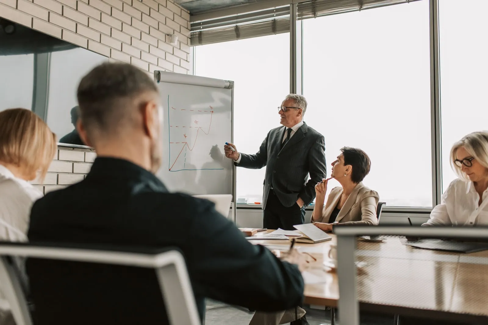 People seated around a table in a meeting room while a man presents at a flip chart