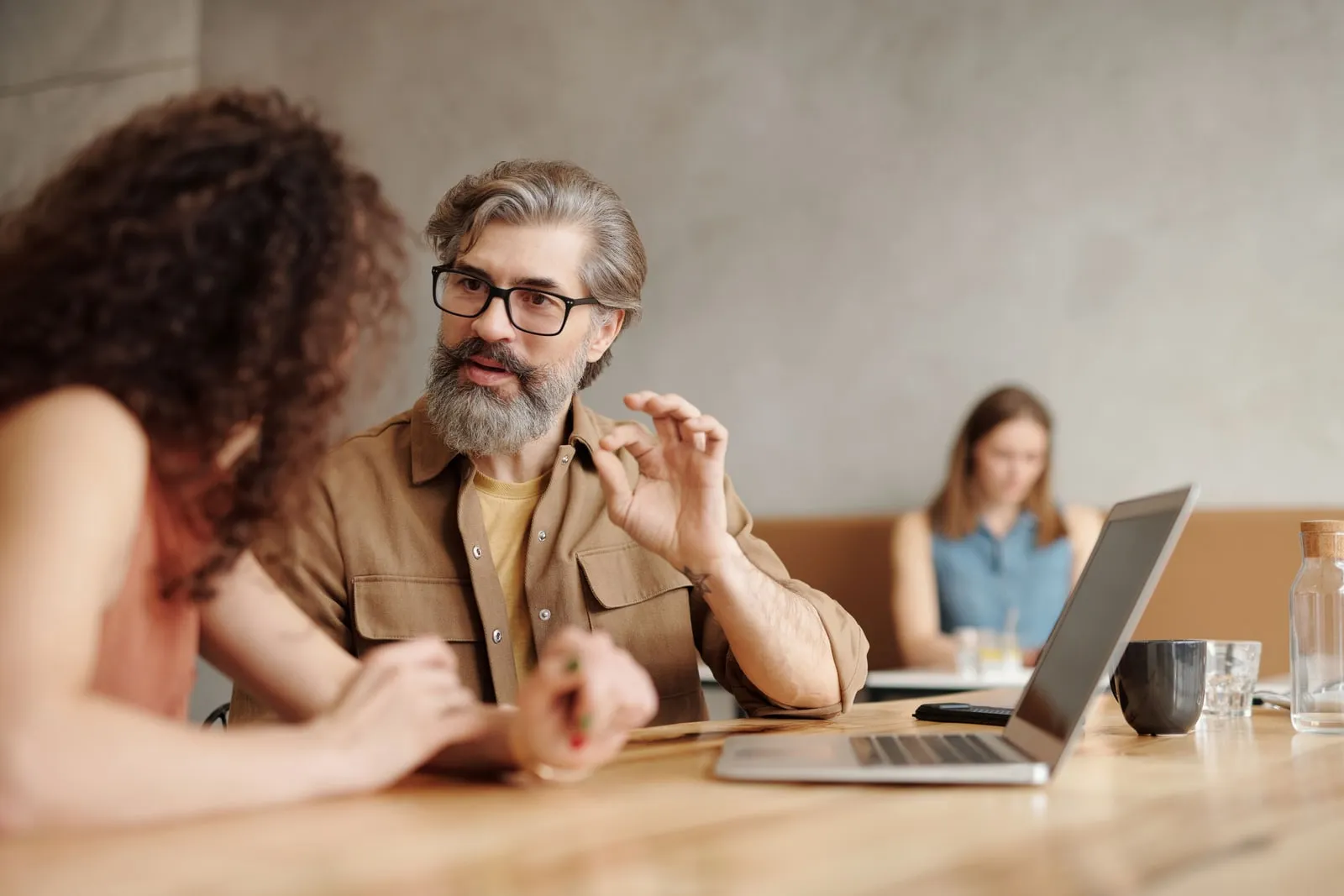 Two colleagues in conversation at a table with a laptop