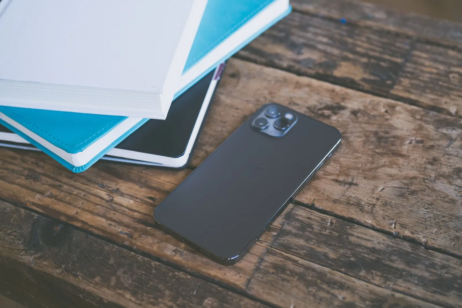 A smartphone lying on a wooden table beside closed notebooks