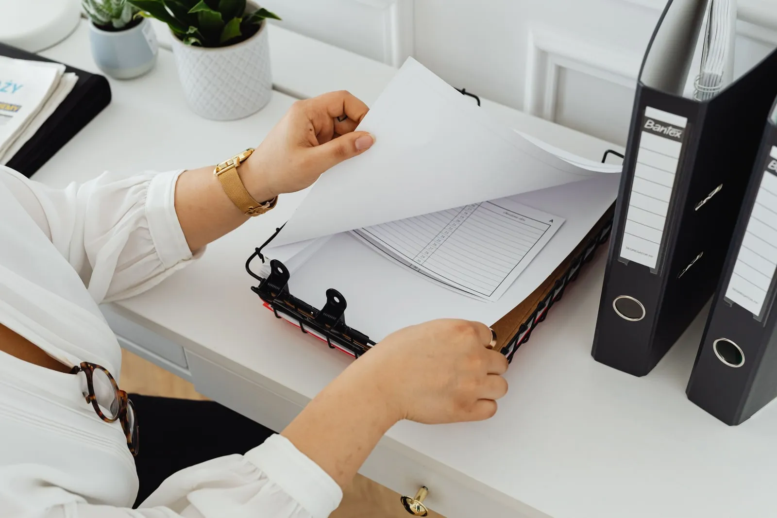 A person sorting papers in ring binders at an office desk