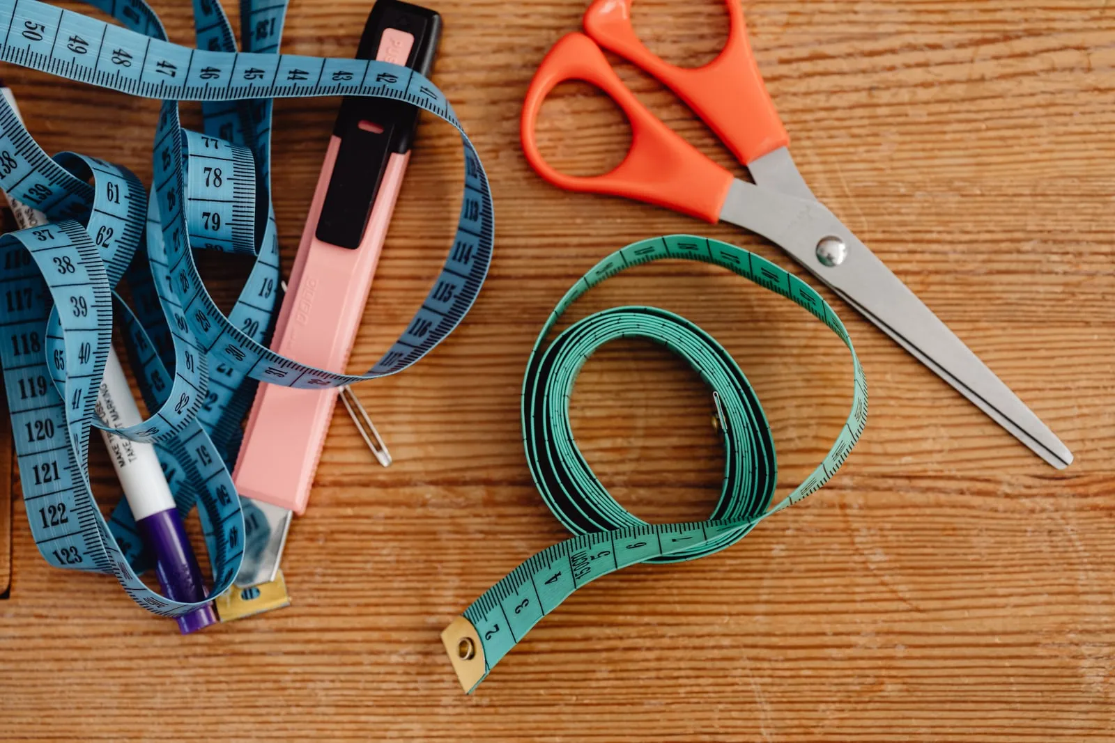 Two tailor's tape measures, a pair of scissors and a marking pen on a wooden table