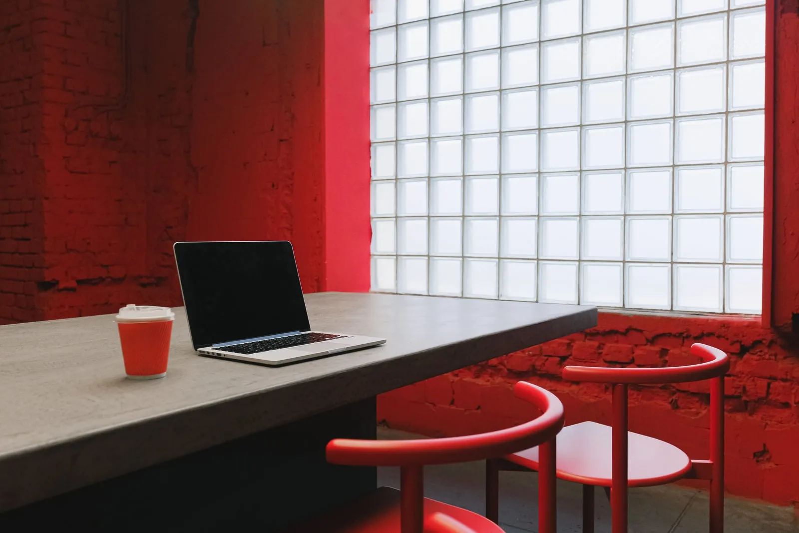 A laptop and a coffee cup on a table by a window, with empty chairs