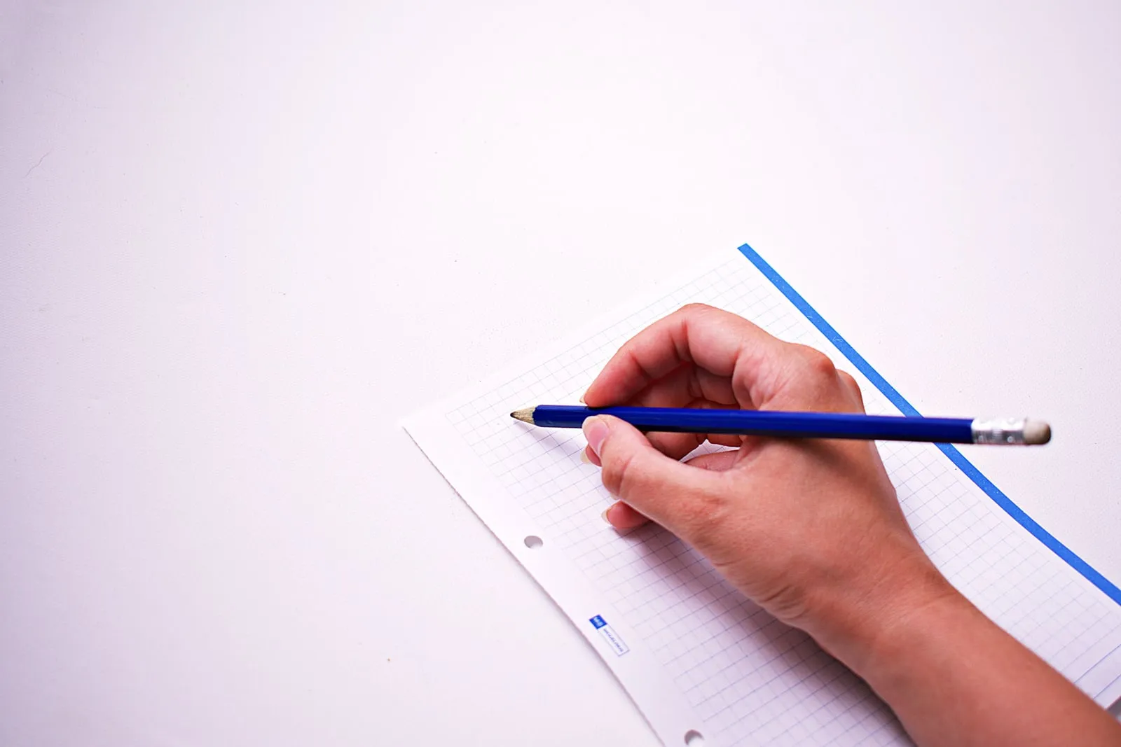 A hand holding a pencil over a sheet of blank graph paper