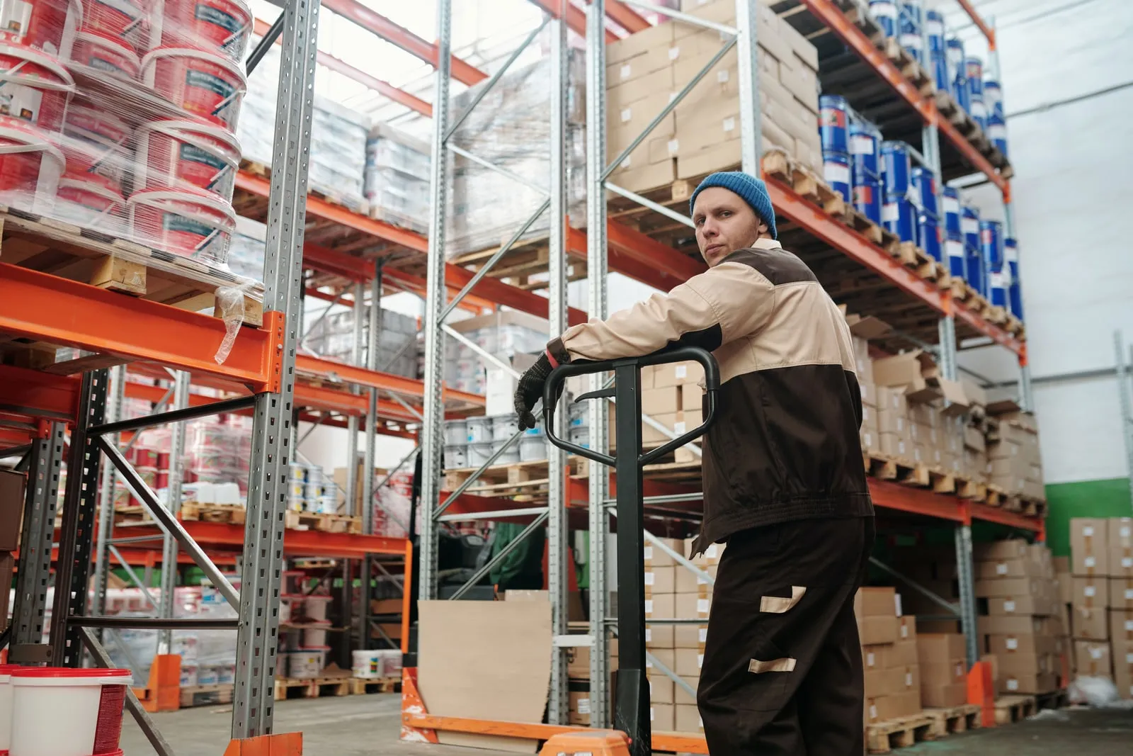 A warehouse worker with a pallet truck beside loaded storage racks