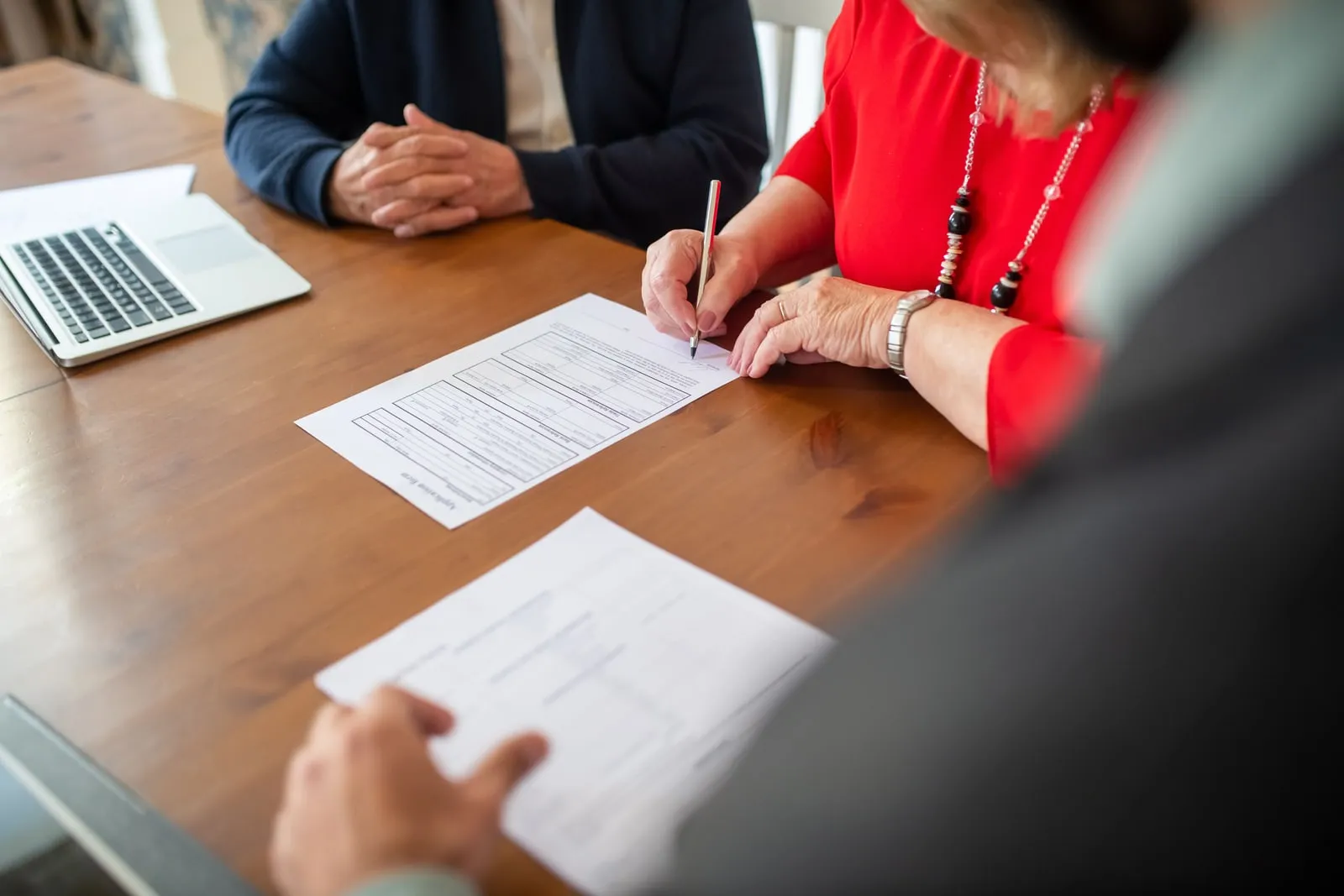 A person signing a document at a table beside a laptop
