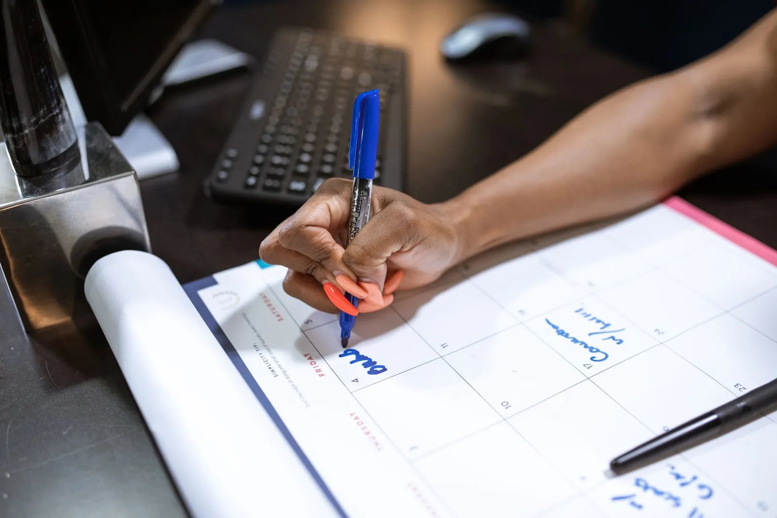 A hand writing on a wall calendar laid out on a desk