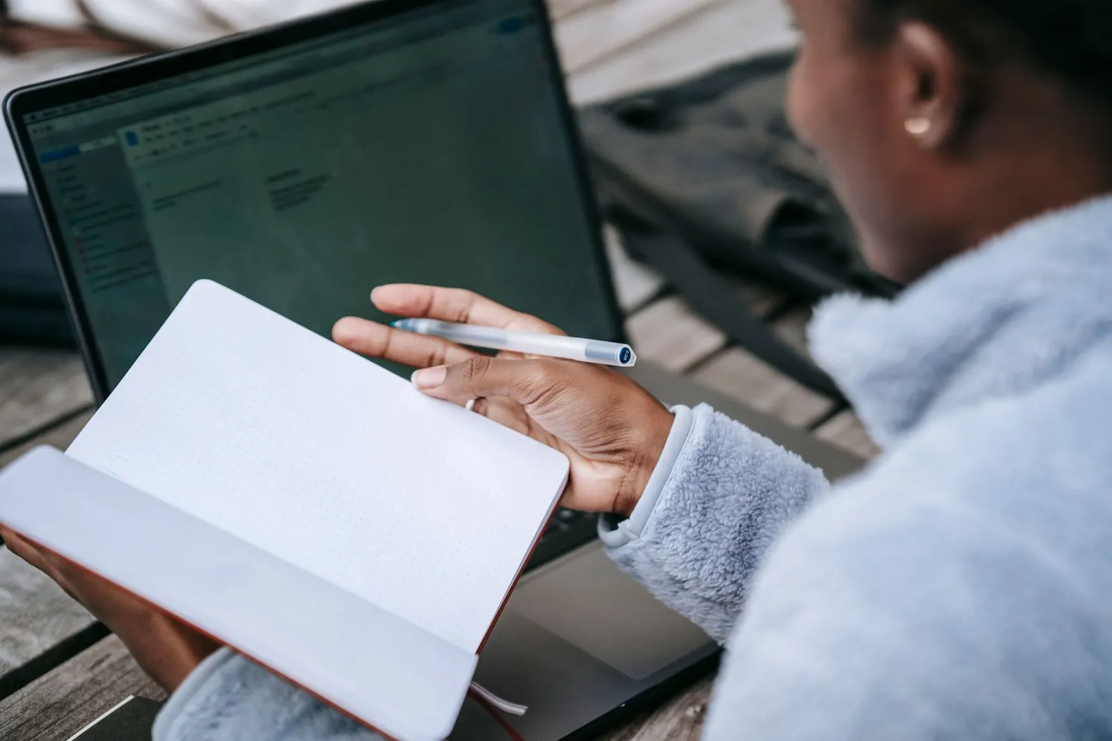 A researcher writing notes in a notebook beside a laptop